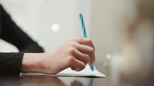 Closeup of hand with writing instrument. Person contemplating with pen and journal in soft warm setting. Artist thoughtfully scribbling ideas in journal during peaceful moment of reflection