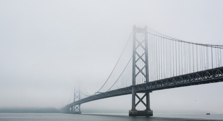 Fototapeta premium Suspension bridge stretches across a body of water during a heavy fog.