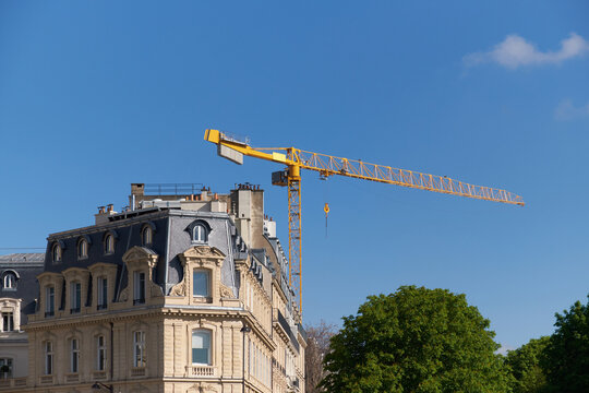 Haussmannian building with yellow construction crane against blue spring sky