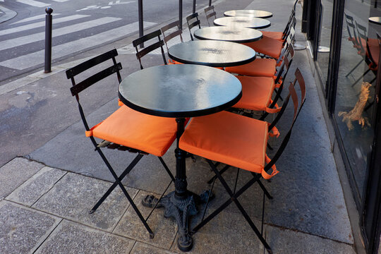 Parisian bistro tables with orange seat cushions on sidewalk cafe terrace