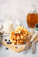 Wooden board of tasty waffles with blueberries and maple syrup on white background