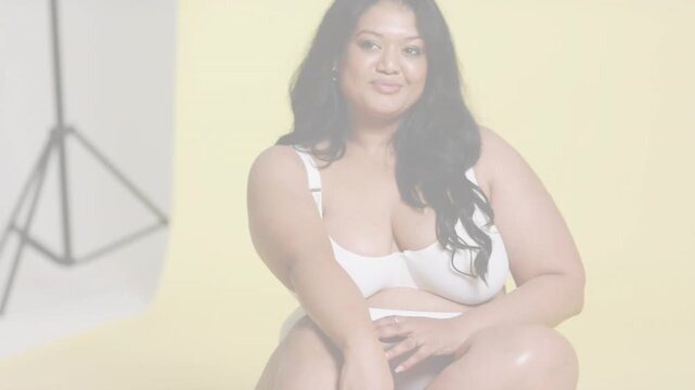 Vertical video: Posing model adjusting pose on seat in yellow set with camera starting wearing bra