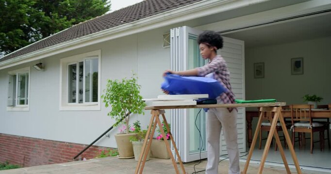 African American woman unfolding blue fabric on patio bench, stretching and using stapler for frame