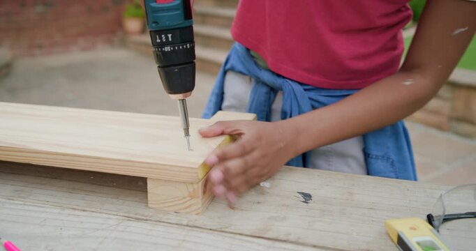 African woman in red tee aligning planks placing screw using drill building platform on patio bench