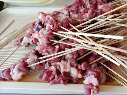 Raw lamb or goat meat satay on bamboo skewers on a tray. Traditional Indonesian sate kambing before grilling. Fresh mutton meat for barbecue and culinary cooking.