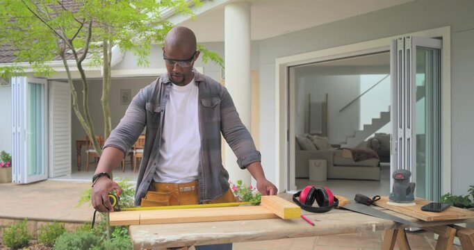 Man adjusting toolbelt, extending tape, checking spacer block, marking plank, sawing for woodwork