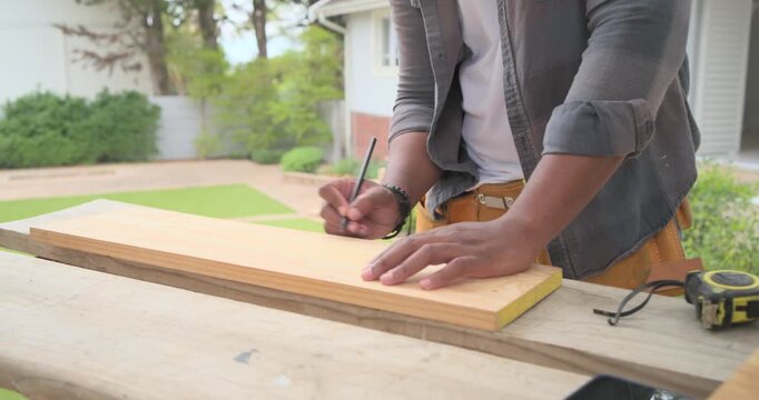 African male measuring, marking, sanding board at bench wearing tool belt with tape measure, sander