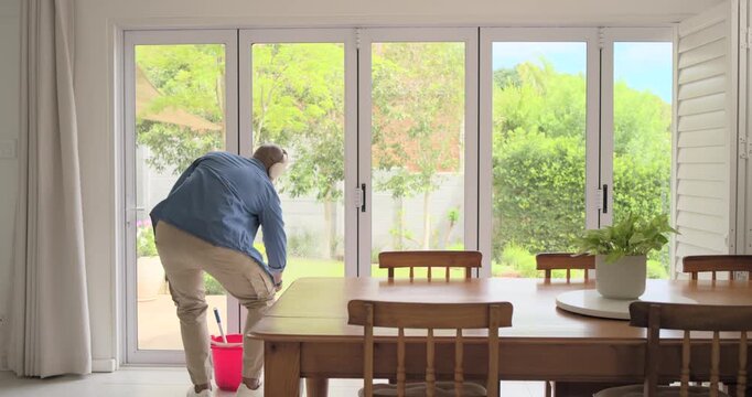 African man reaching red bucket, dipping squeegee, cleaning sliding door in dining area, copy space