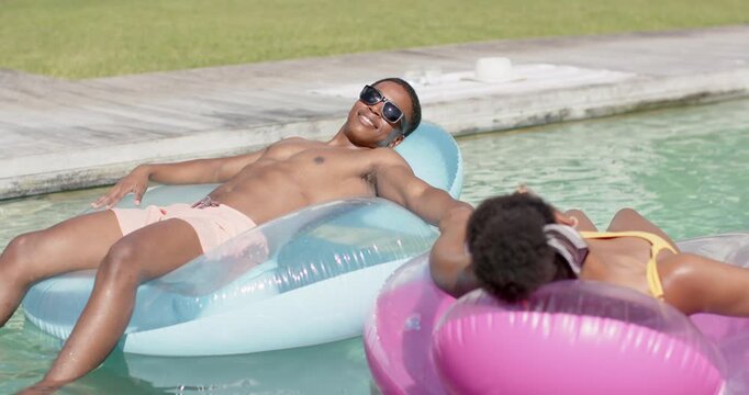 Man reclining blue lounger, woman on pink donut float reaching and holding hands for lifestyle ads