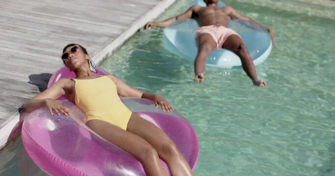 Woman reclining on pink float adjusting shades for ad, camera pulling back as man reaching deck