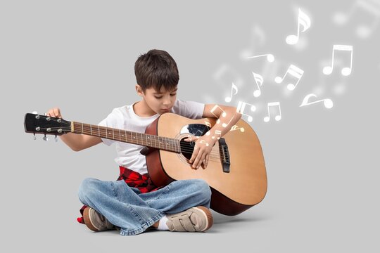 Little boy playing guitar on grey background