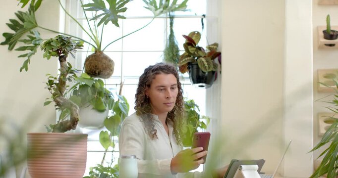 Nonbinary African American sitting at desk by window checking red phone tapping tablet using laptop