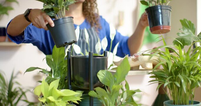 Nonbinary person aproned lifting pot from left placing two pots into planter stand, organizing shop