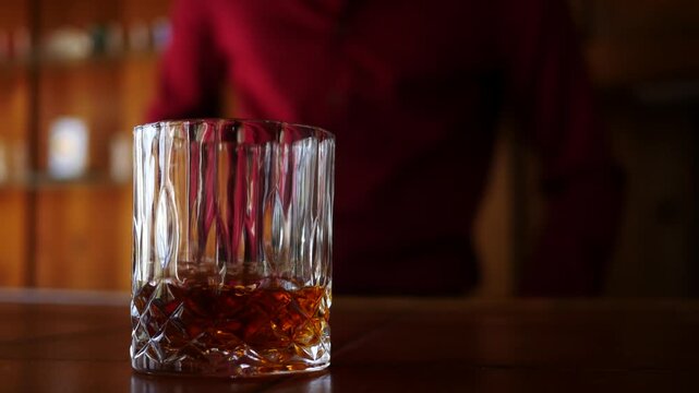 Male Bartender sets down a Glass of Whiskey in Trendy Bar