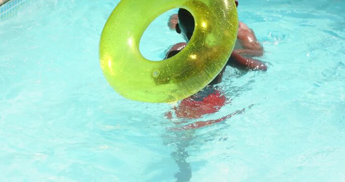 Raising arms shirtless adult playfully splashing boy in red trunks at pool with green float ring