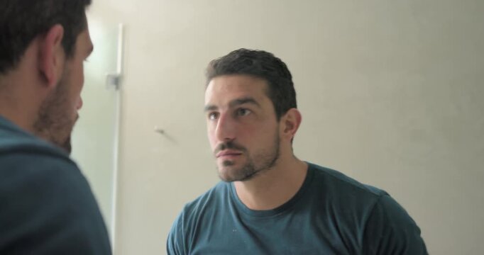 30s man touching lip, leaning into bathroom mirror, checking stubble and grooming with wristband