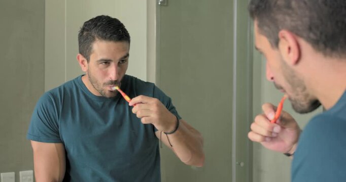 Man raising orange brush, brushing teeth and watching bathroom mirror, checking form with wristband