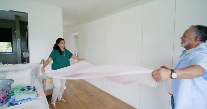 African American couple, woman picking up pale pink sheet, folding to remove wrinkles in bedroom
