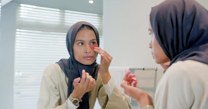 Adult female choosing red undereye patch inspecting mirror applying from jar at sink for skincare
