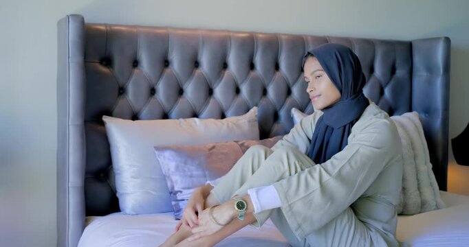African American woman wearing hijab sitting on bed noticing camera moving shifting gaze smiling