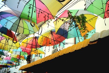 A vibrant display of multi-colored umbrellas is suspended in the air, creating a festive overhead canopy. © endang
