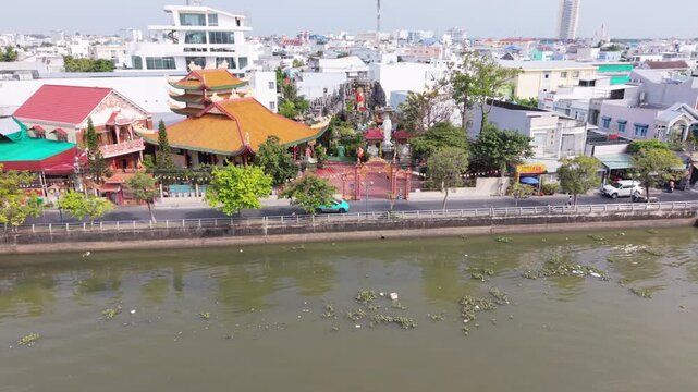 Can Tho Riverbank Temple Scene. Tranquil Asian Temple Alongside Muddy River With Lotus Gardens. Peaceful Riverside Temple In Can Tho Featuring Orange Roofs And Blooming Lotus Patches