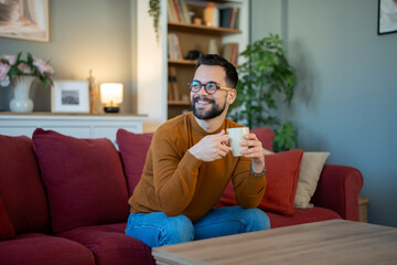 Obraz premium Man relaxing on sofa enjoying morning coffee at home