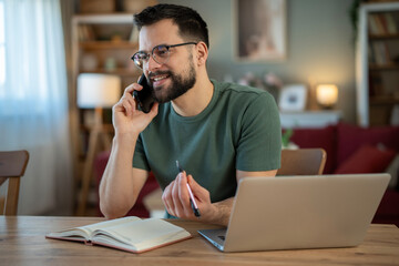 Fototapeta premium Young man working from home talking on phone