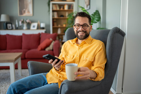 Happy man relaxing at home holding phone and mug