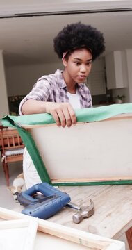 Vertical video: Pulling green cloth, woman in plaid smoothing and stapling wood frame at doorway