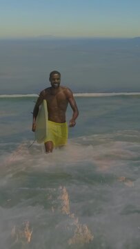 Vertical video: Surfer after ride, walking to shore, overlay flagging broken fins on yellow board