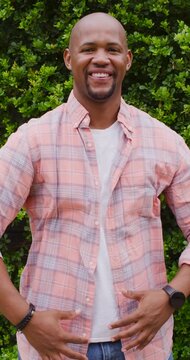 Man uncrossing arms and adjusting plaid shirt and jeans against green hedge, preparing fashion pose
