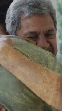 Vertical video: Senior man hugging son after return, patting back and speaking by window for family