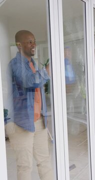 Vertical video: Grabbing handle man in denim shirt checking, cleaning glass door at home with mop