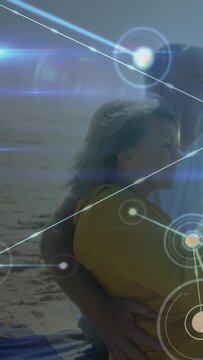 Vertical video: Seniors sitting sand, sun sparking nodes and rings linking around them for tech