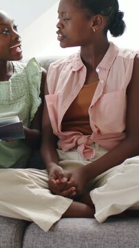 Vertical video: Turning teen in pink shirt responding to child showing open book at home, smiling