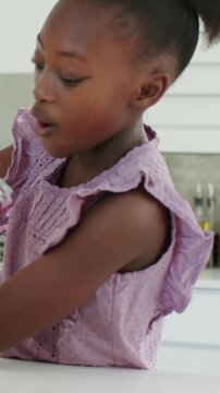 Vertical video: Reaching kid in lilac top at kitchen sink, reacting to faucet splash, resuming task