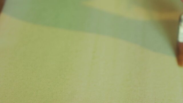 Close-up of a hand using a brush to apply paint or base layer on paper, capturing a quiet artistic process with soft textures and minimal composition.