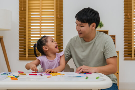 cheerful father and child girl drawing and painting with colorful oil pastels on paper