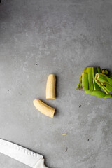 Overhead view of sliced unripe plantains on grey countertop, top view of peeled green plantains in a white bowl on a grey background, unripe plantains being prepared and sliced for cooking © this_baker
