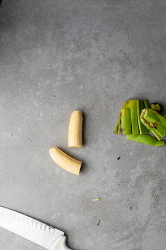 Overhead view of sliced unripe plantains on grey countertop, top view of peeled green plantains in a white bowl on a grey background, unripe plantains being prepared and sliced for cooking
