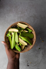 overhead view of green plantain peels in a woven basket on a grey countertop, top view of unripe plantain or banana peels in a basket on a textured grey background © this_baker