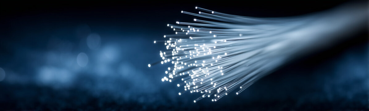 Fiber Optic Filament in the Focus: Close-up of a bundle of illuminated fiber optic filament, representing the core of data transfer with a soft, ambient glow on a textured, dark backdrop. 