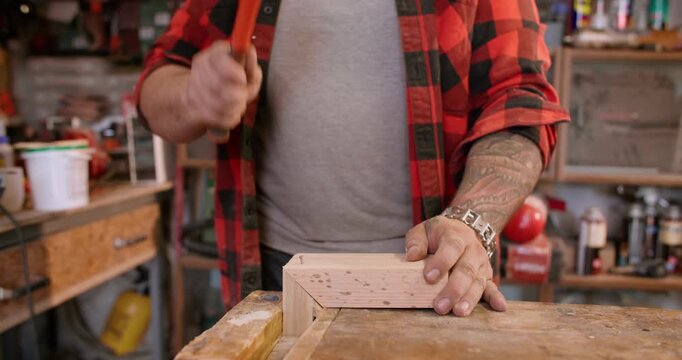 Carpentry workflow. Hammering nail. Man in plaid skirt assembling furniture part on wooden table. Joiner hand tool service industry.