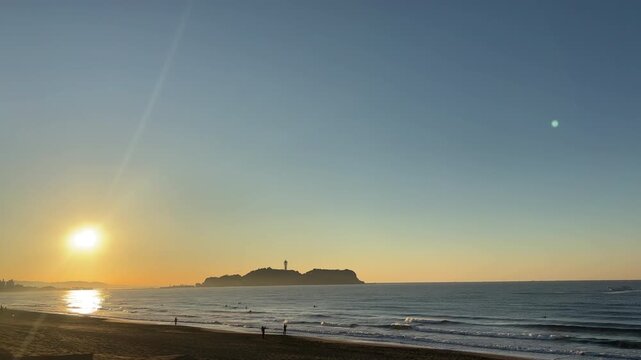 日の出と朝焼けと青空の調和した江ノ島に打ち寄せる穏やかな波