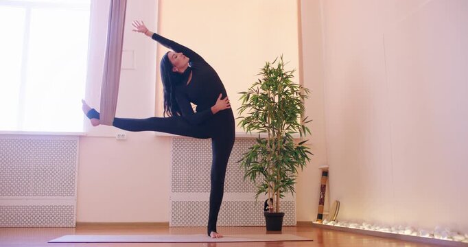 Flexibility activity. Fitness studio. Female doing side stretch in split pose with leg support on fly yoga hammock for spine strength.
