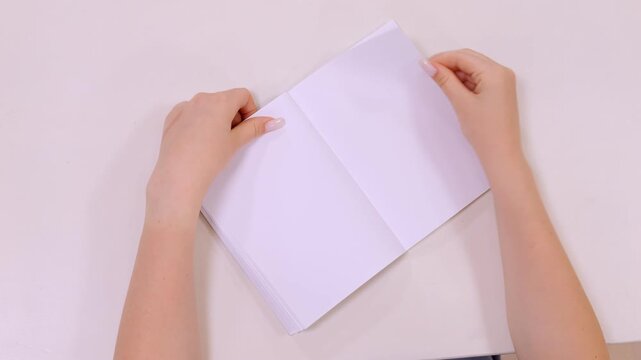 Hands open blank notebook on plain white surface. Minimalist scene with clean, soft lighting. Focus on gentle action and empty pages. Perfect for creative, educational, or planning themes