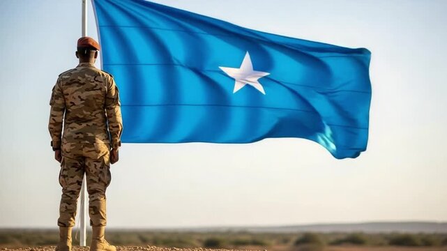 Somali Soldier in Camouflage Uniform Standing at Attention Before National Flag