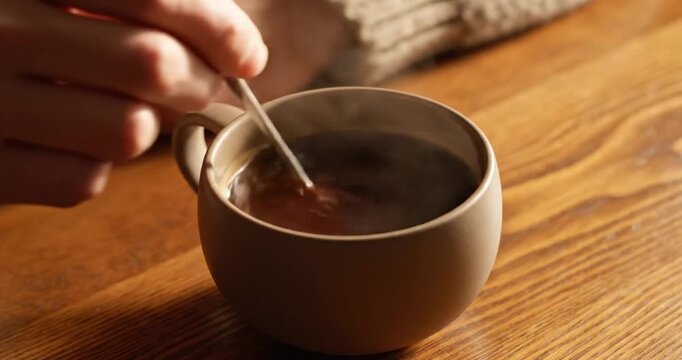 A person stirring a warm beverage in a cozy setting with wooden table and soft lighting