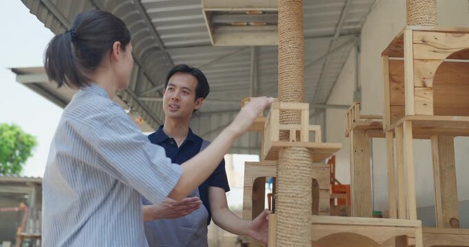 Entrepreneur and carpenter review wooden furniture mockup and prototype pieces, discuss design details and inspect quality at a small business workshop during product development.
